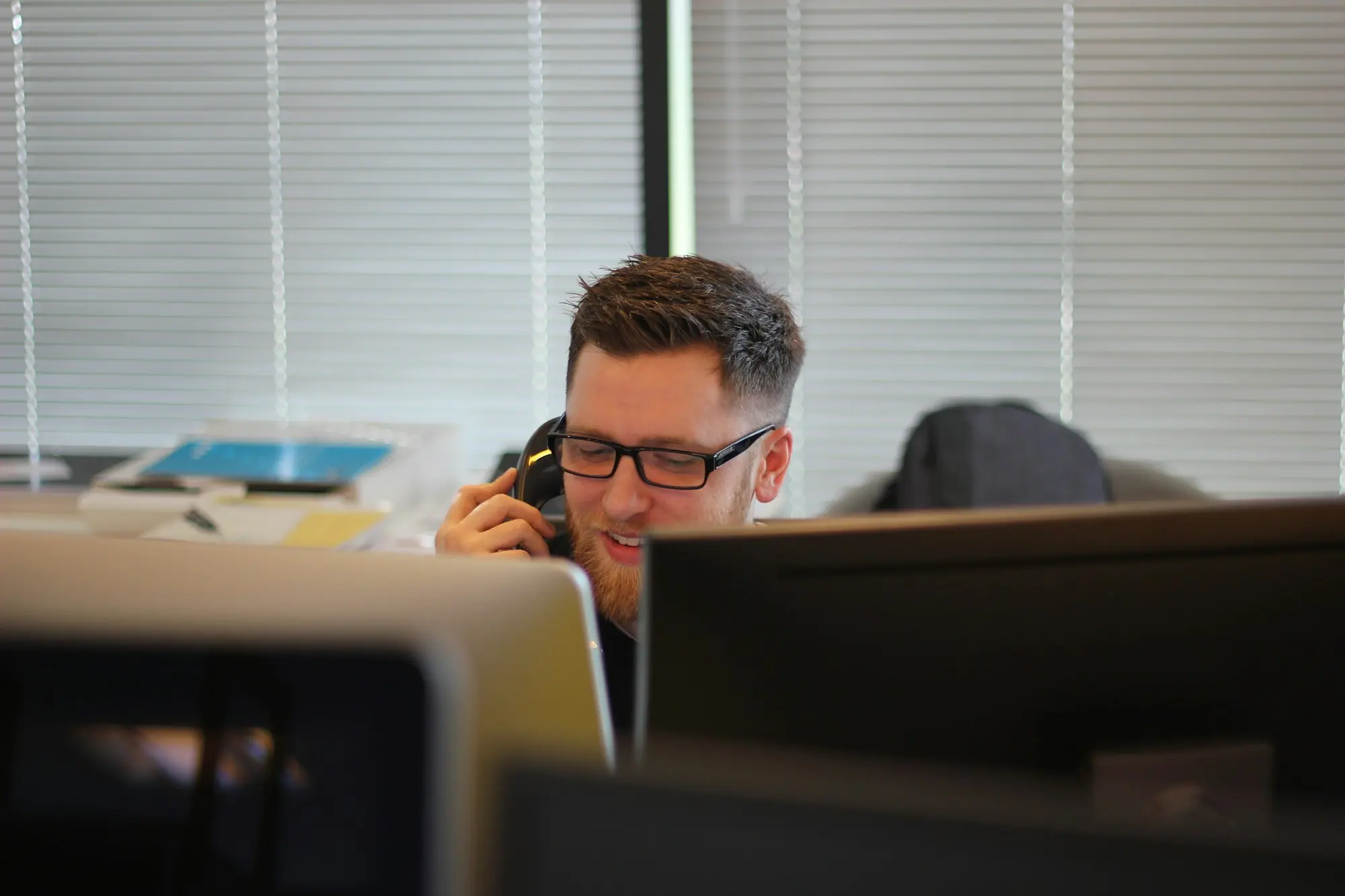 A man at his desk taking a call on an office phone.