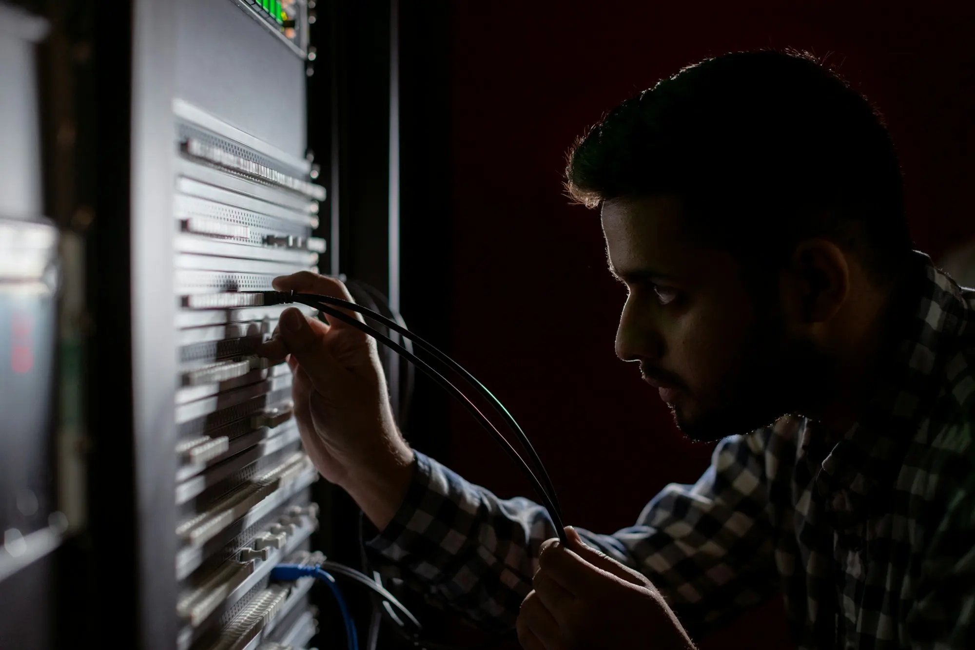 A technician in a plaid shirt patching cables into a rack of network equipment.