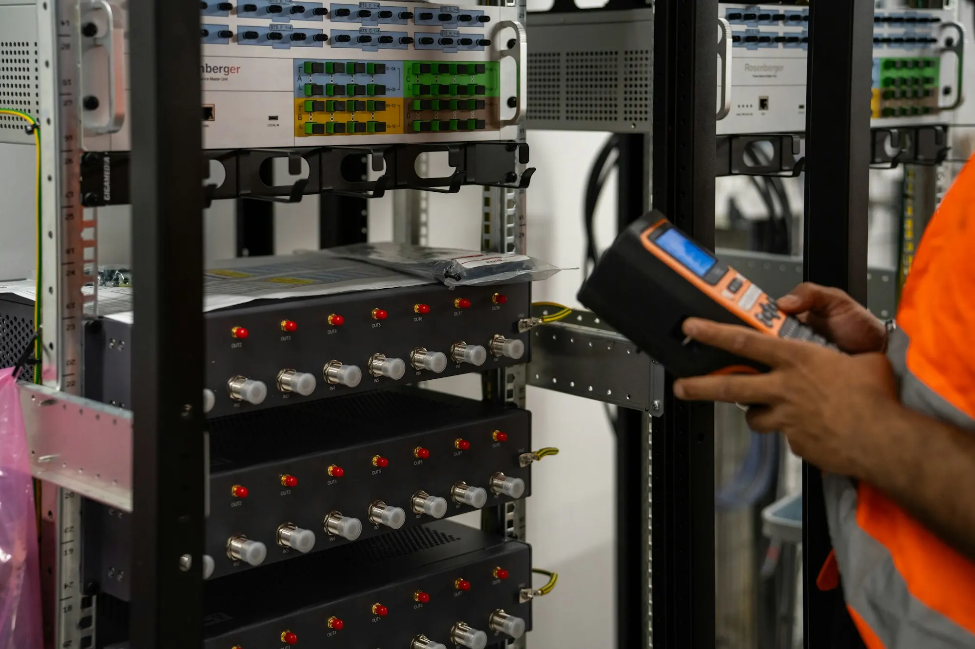 A technician in a high-visibility vest checking a server rack with a handheld tester.